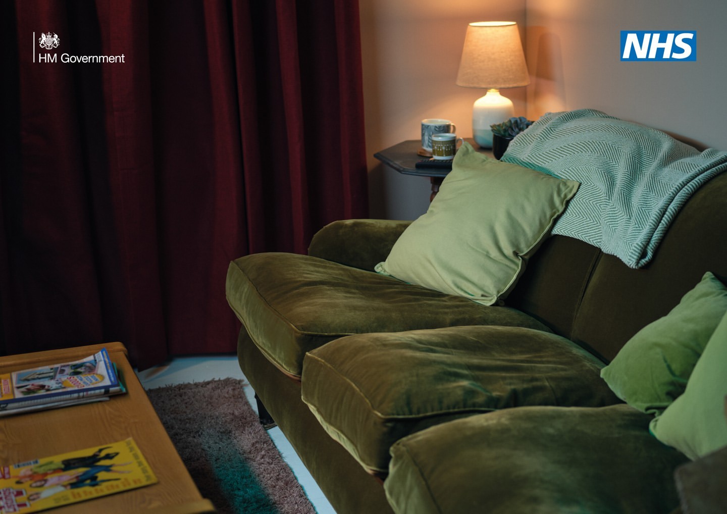 Interior shot of a living room scene with an olive green couch with sage green pillows and a teal throw blanket, creating a warm, inviting space.
