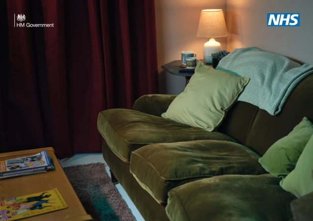 Interior shot of a living room scene with an olive green couch with sage green pillows and a teal throw blanket, creating a warm, inviting space.