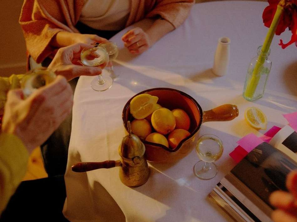 Overhead view of a table set for an intimate gathering with lemons, drinks, flowers, and magazines; warm, inviting ambiance.