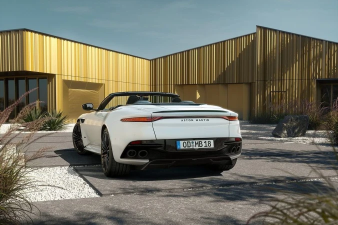 Rear view of a white Aston Martin convertible parked in front of a modern golden building, showcasing its sleek design.