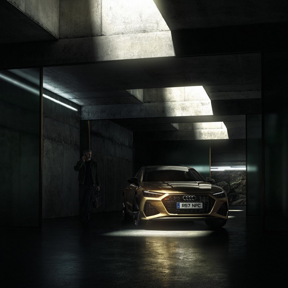 Gold Audi RS7 parked in a concrete structure with a man in the background using a phone, emphasizing automotive and urban photography.