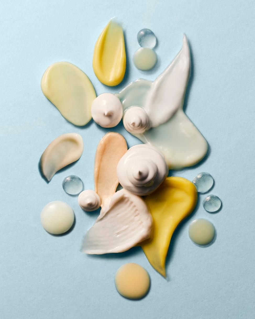 Macro studio shot of assorted cosmetic cream and lotion textures in pastel shades against a light blue background, ideal for beauty ads.