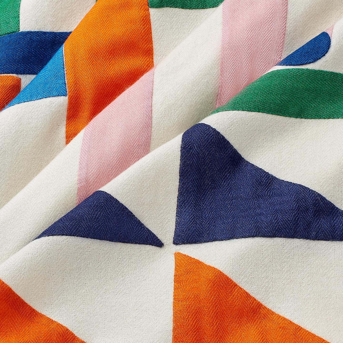 Close-up of a folded fabric with geometric triangle pattern in blue, orange, pink, green, and white creating a visually striking textile design.