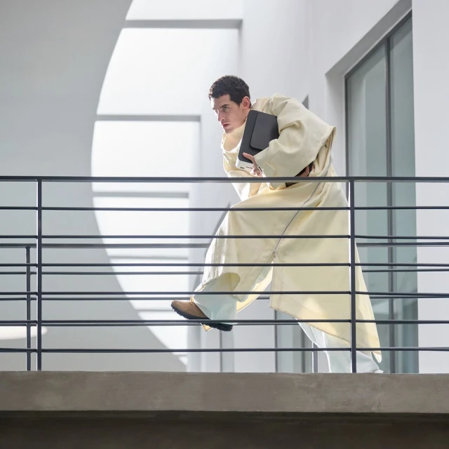 Man in robe runs on balcony indoors holding folder with sunlight and architectural elements providing a dynamic composition.