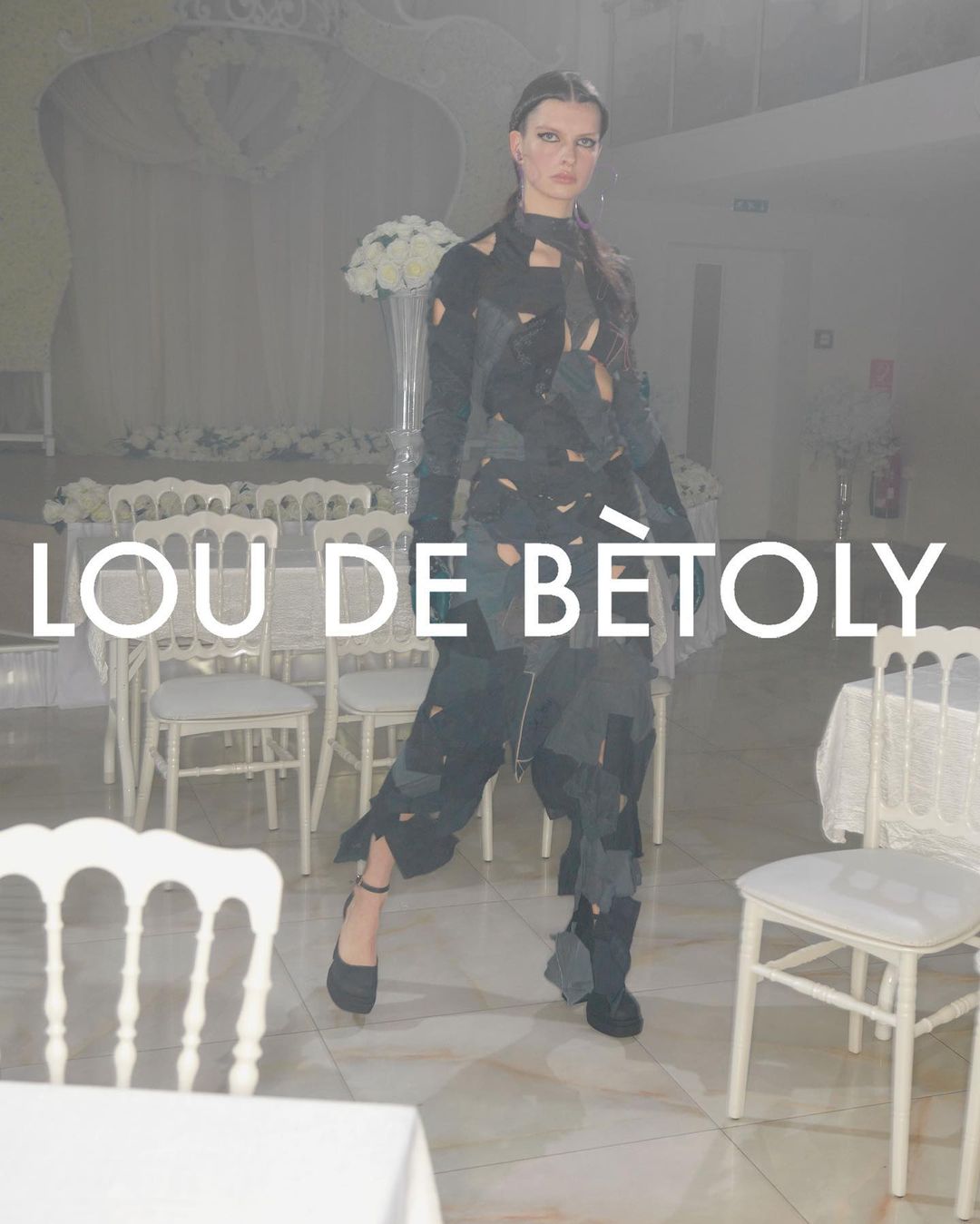Fashion model poses in a unique cut-out garment at an event with white chairs and flowers, spotlighting avant-garde style.