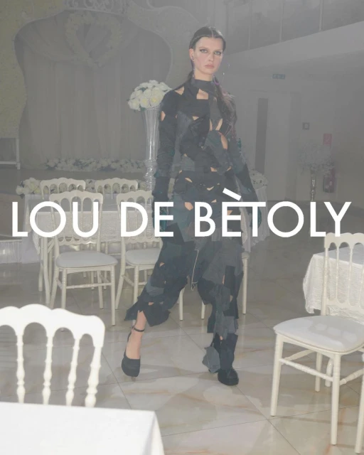 Fashion model poses in a unique cut-out garment at an event with white chairs and flowers, spotlighting avant-garde style.