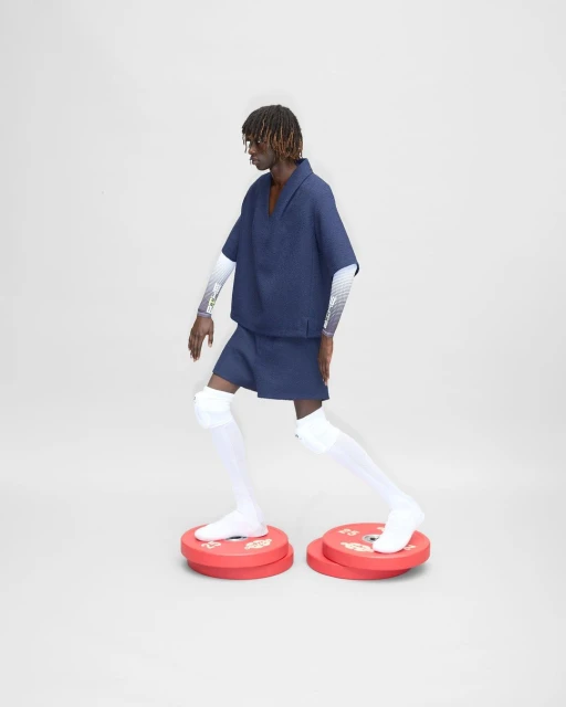 Editorial fashion shot of a Black male model wearing a blue outfit and white knee socks, standing on red exercise plates against a white backdrop.