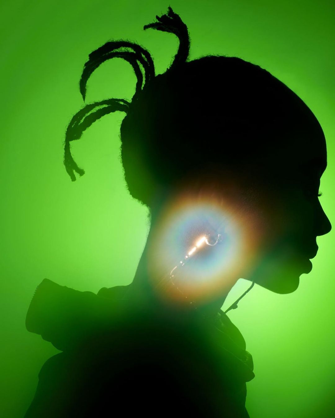 Silhouette of a young adult with braided hair on a bright green background, highlighted with lens flare, showcasing profile and hairstyle.