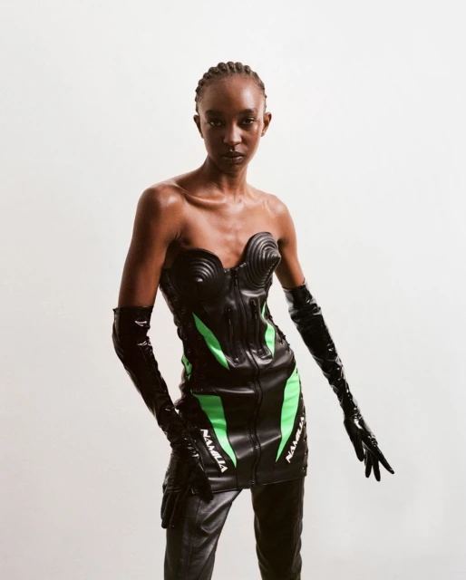 Fashion shot of a slender Black female model in a black futuristic bodysuit with neon green accents, black gloves, and black pants posing.