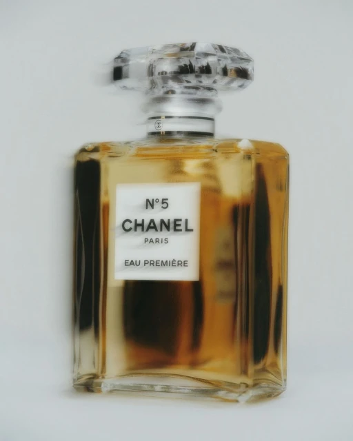 An amber-tinted Chanel N°5 Eau Première perfume bottle is centered on a light background, featuring a clear faceted stopper.