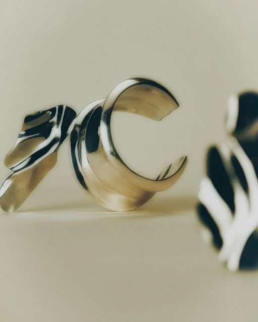 Abstract still life featuring chrome metal and striped resin shapes against a pale background, rendered with a shallow depth of field.