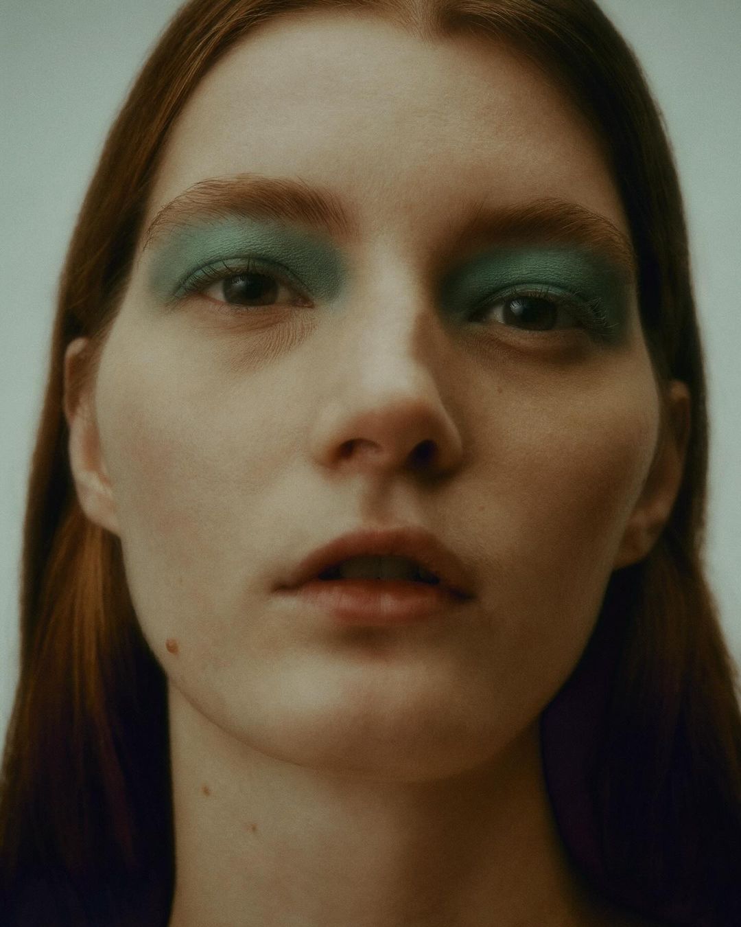 Close-up portrait of a woman with green eyeshadow and parted lips against a neutral background by Troy Covey