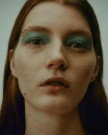 Close-up portrait of a woman with green eyeshadow and parted lips against a neutral background by Troy Covey