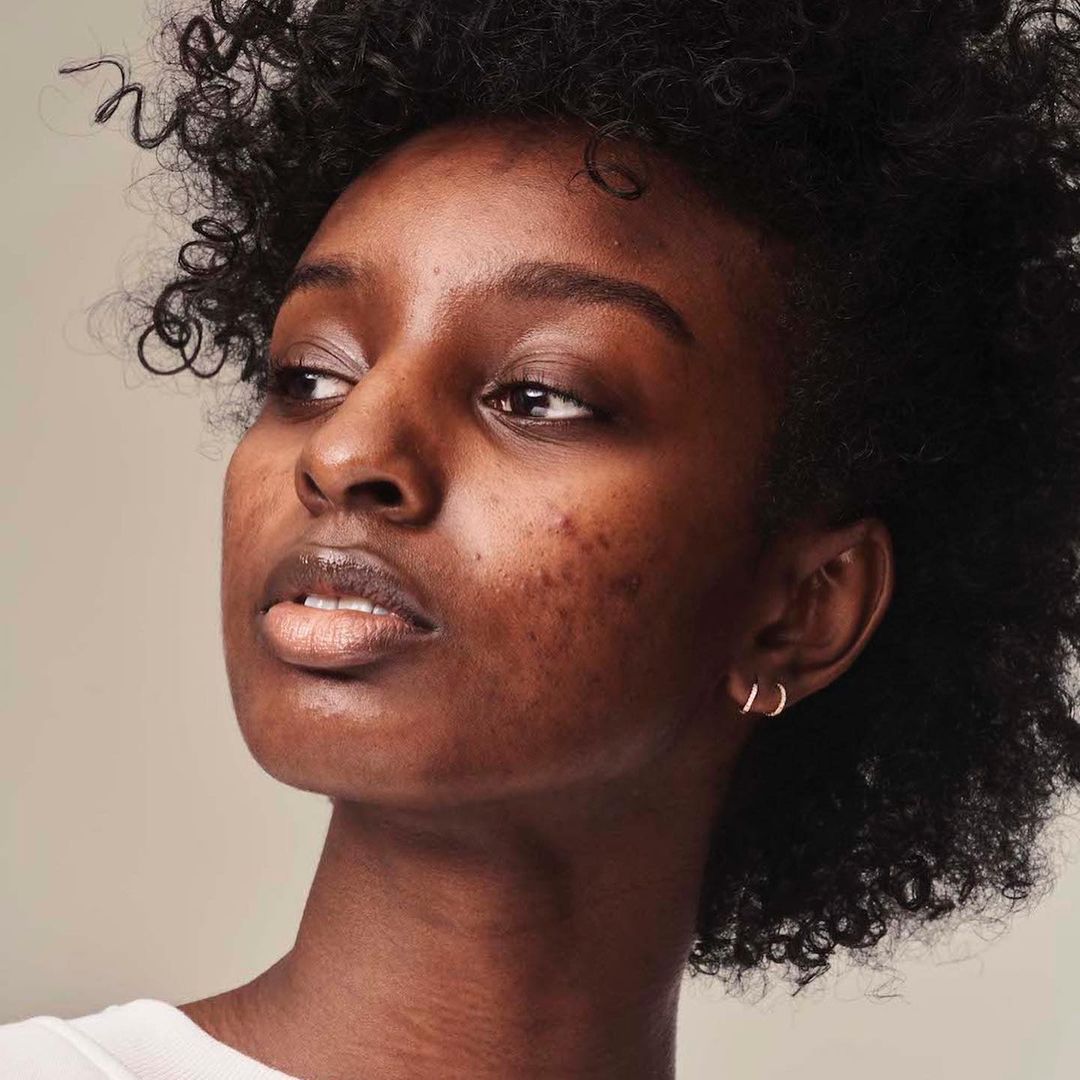 Close-up portrait of a young adult African-American woman with curly hair, looking off-camera against a neutral background.