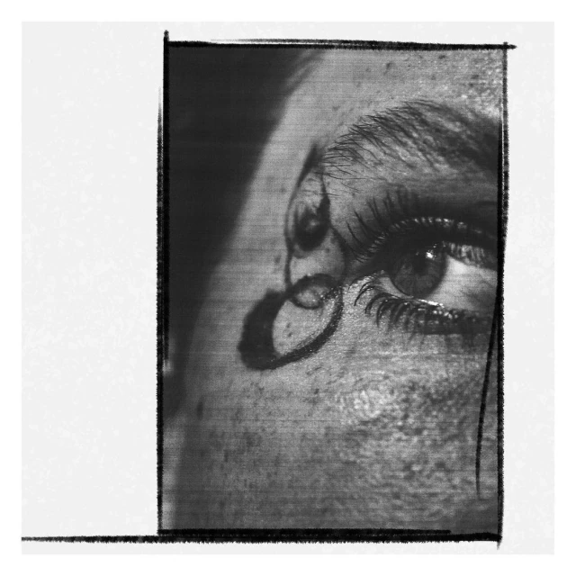Black and white close-up of an adult human eye and eyebrow, featuring visible eyelashes, textured skin, and distinct shadowing.
