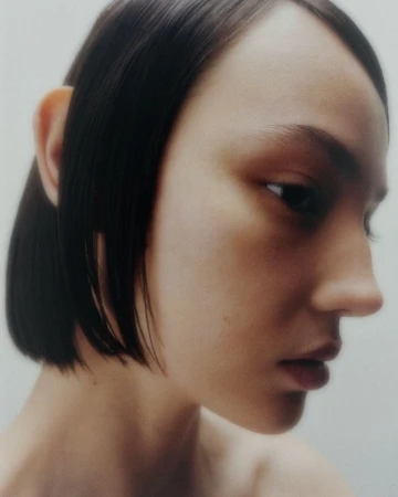 Close-up profile portrait of a model with short dark hair against a plain light background by Troy Covey.