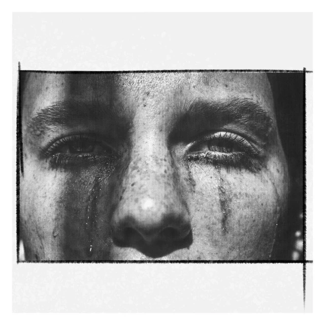 Close-up black and white portrait of a person with tear-like streaks down their face, captured in a framed composition with natural light.