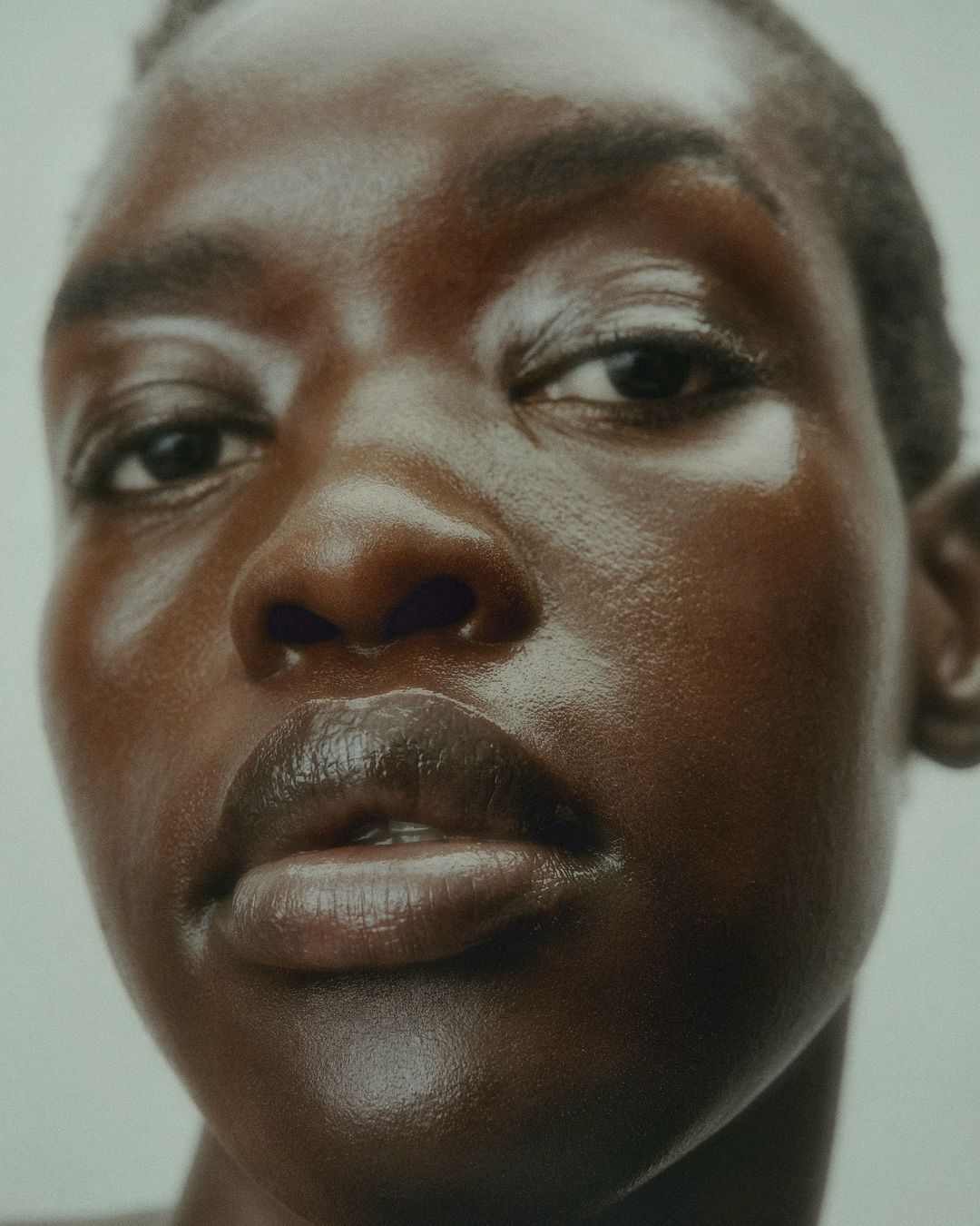 Close-up beauty shot of a woman with brown skin and a short haircut. The lighting is soft, emphasizing the skin's smooth texture.