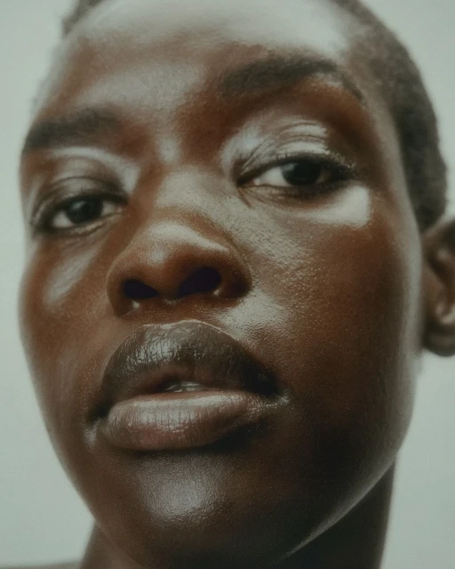 Close-up beauty shot of a woman with brown skin and a short haircut. The lighting is soft, emphasizing the skin's smooth texture.