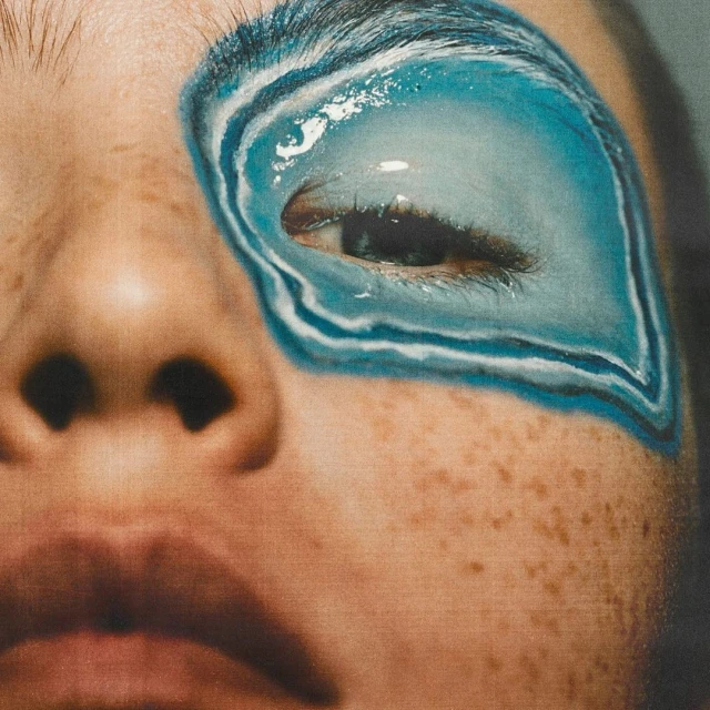 Close-up of a fair-skinned person with blue and white eye makeup extending from the eyelid to the eyebrow, highlighting artistic detail.