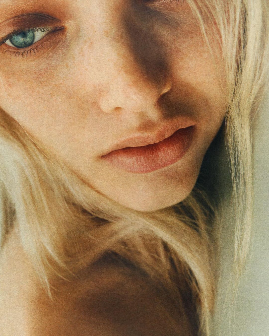 Close-up portrait of a fair-skinned woman with blonde hair and striking blue eyes, softly lit with focus on her natural features.