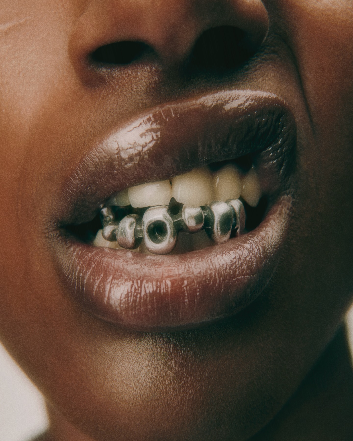 Close-up of a Black woman's mouth with silver tooth jewelry, showcasing glossy lips and dental accessories in a beauty or fashion context.