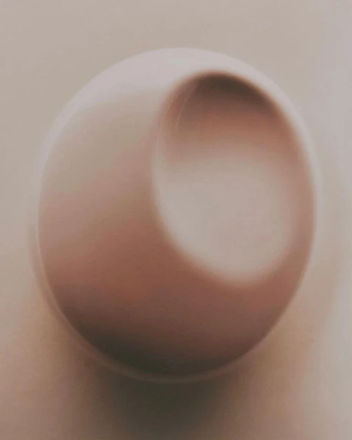 Abstract close-up of a white sphere with a concave indentation, soft lighting and shadows create a minimalist, three-dimensional effect.