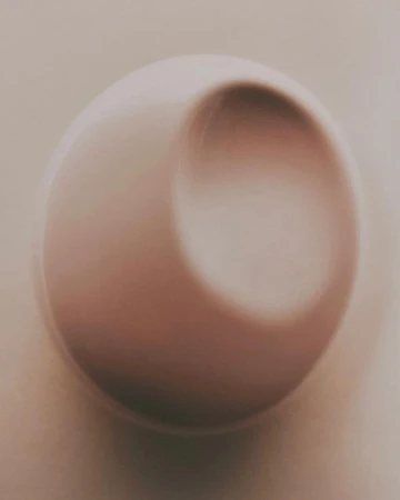 Abstract close-up of a white sphere with a concave indentation, soft lighting and shadows create a minimalist, three-dimensional effect.