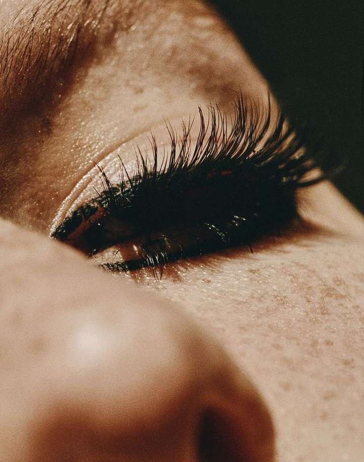 Macro close-up of a person's eye with long, dark eyelashes against a dark background emphasizing detail and texture.