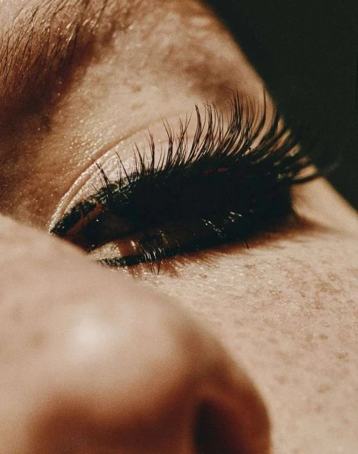 Macro close-up of a person's eye with long, dark eyelashes against a dark background emphasizing detail and texture.