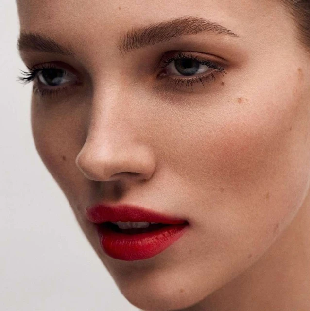 Close-up portrait of a fair-skinned woman with red lipstick, showcasing makeup and beauty in a studio setting with neutral background.