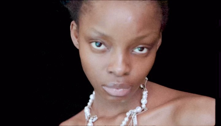 Close-up portrait of a woman with dark skin and pearl necklace against a black background in a studio setting.