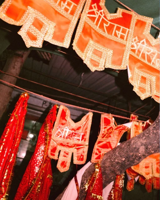 Outdoor display of orange religious banners with white lettering strung from a tree branch, creating a vibrant and spiritual atmosphere.