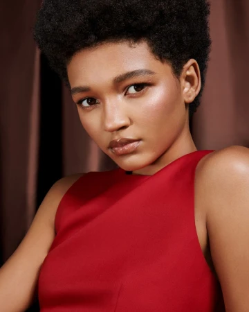 Close-up portrait of a woman with short dark hair wearing a sleeveless red top against a brown backdrop