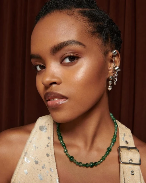 Close-up of a young woman with tan skin wearing a halter top and green beaded necklace, adorned with silver ear cuff jewelry.