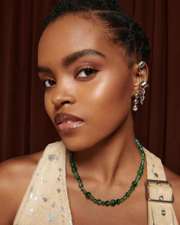 Close-up of a young woman with tan skin wearing a halter top and green beaded necklace, adorned with silver ear cuff jewelry.