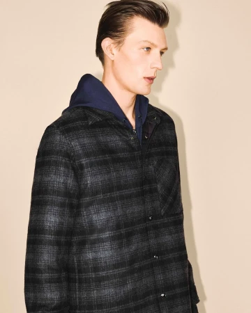 Portrait of a man wearing a plaid jacket and navy blue hoodie against a plain beige background