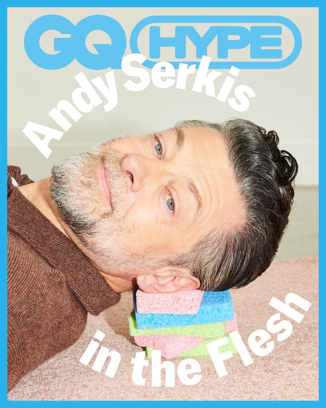 Andy Serkis lays on a colorful sponge-stack for GQ Hype cover. He wears a brown sweater, has graying hair, and a blue-bordered frame.