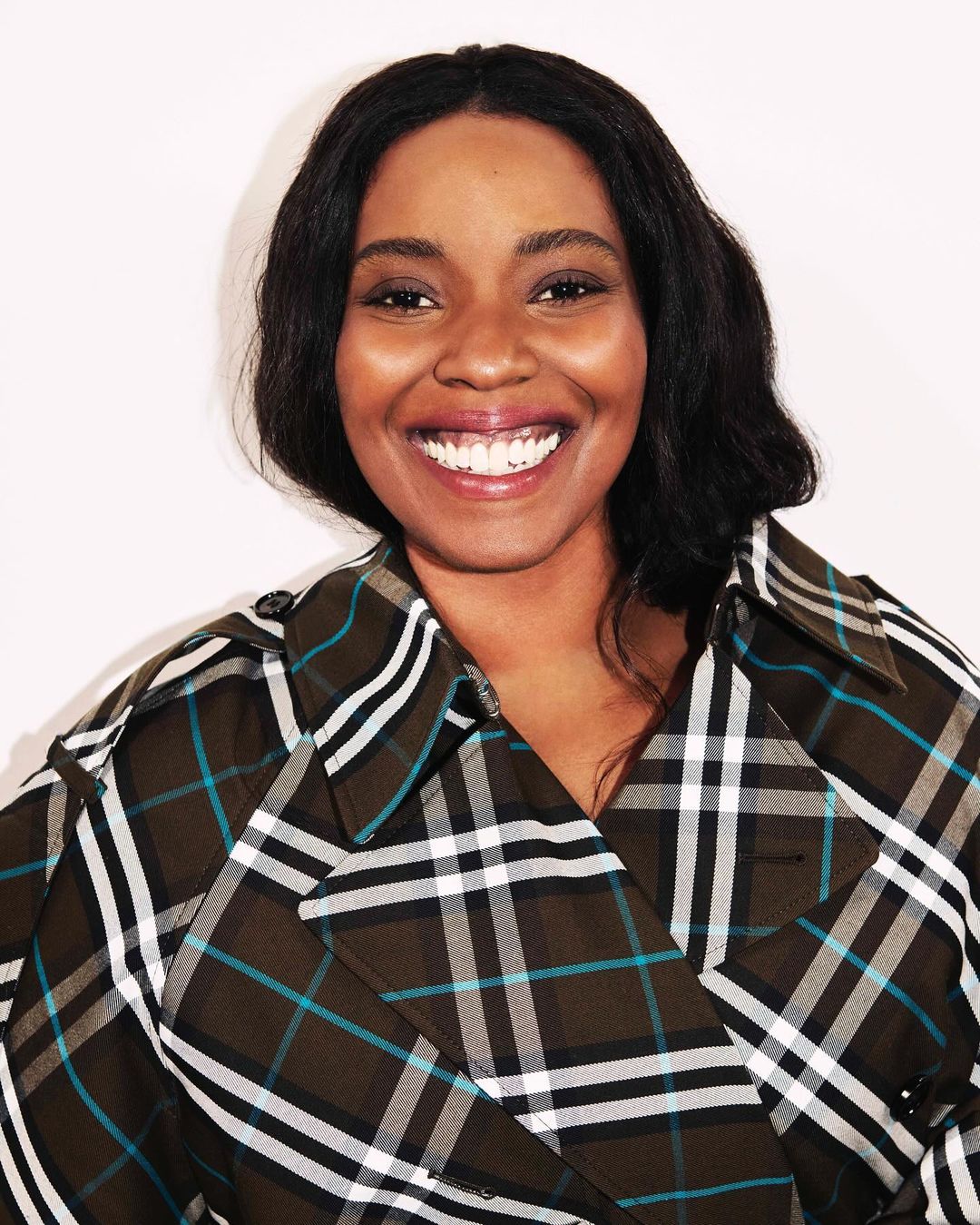Portrait of smiling Black woman wearing a plaid trench coat against white background