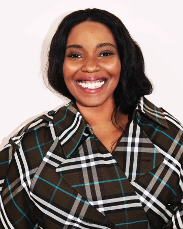 Portrait of smiling Black woman wearing a plaid trench coat against white background