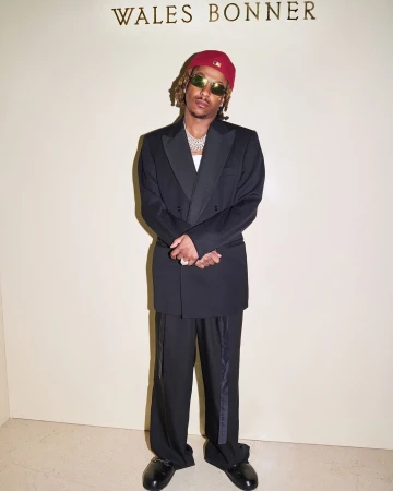 Man in a black tuxedo and red beanie standing in front of a wall with Wales Bonner branding in London.