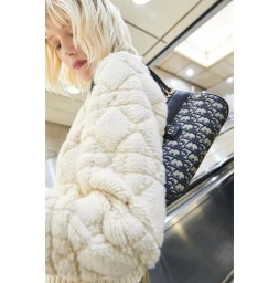 Blonde woman wearing a textured cream sweater carrying a patterned shoulder bag on an escalator by Tung Walsh