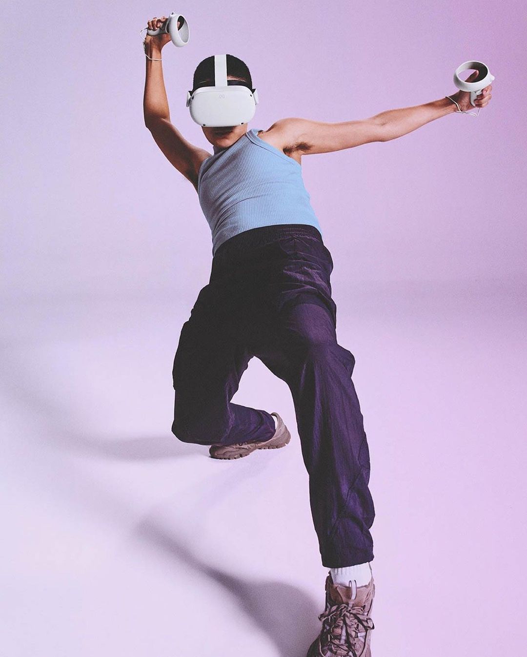 Adult wearing a VR headset and holding controllers in a studio with a light purple background, focused on tech and gaming.