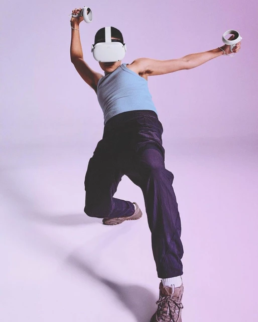 Adult wearing a VR headset and holding controllers in a studio with a light purple background, focused on tech and gaming.