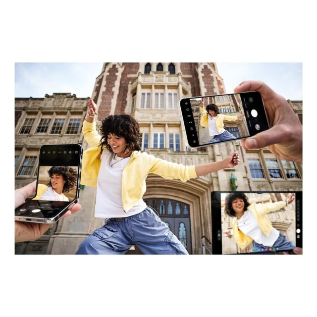 Young woman in blue pants and yellow jacket dances with arms outstretched, framed by hands holding smartphones capturing the moment.