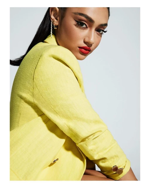 Close-up fashion portrait of a woman with red lipstick wearing a yellow blazer against a neutral background in a photo studio.