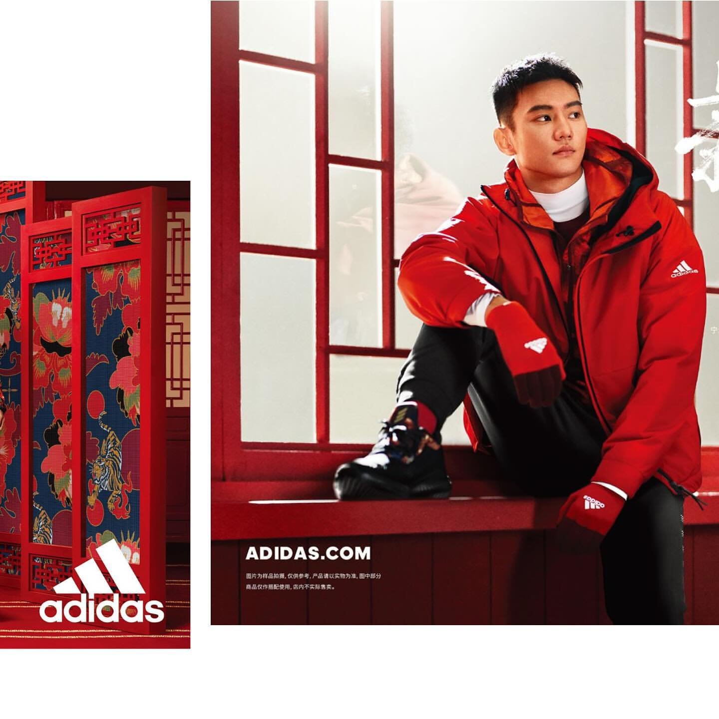 An Asian adult male model poses in red Adidas winter clothing, seated indoors against a red frame wall and Adidas logo. Adidas promotion.