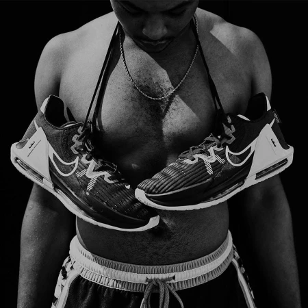 Shirtless man wearing athletic shorts with sneakers hung around his neck by their laces against a black background