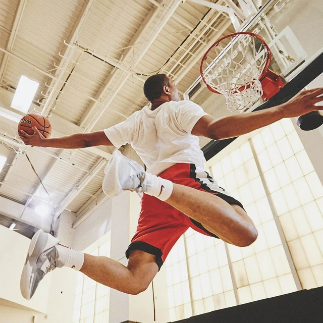 A basketball player in mid-air with a basketball, ready to dunk, in a gymnasium with a high-angle shot capturing dynamic action.