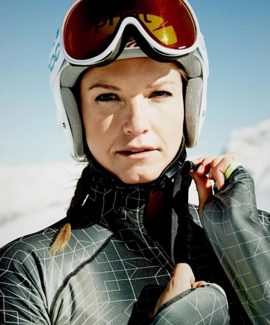 Close-up of adult female skier in helmet adjusting jacket against snowy mountain backdrop on a bright, sunny day.